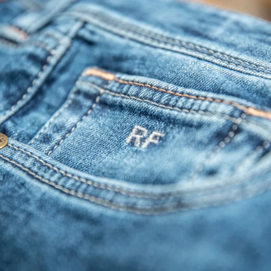 Close-up of blue denim with embroidered initials and pocket stitching