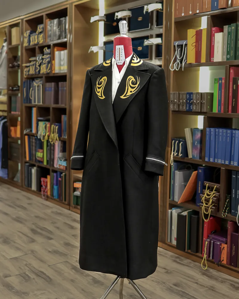 Dark overcoat with gold embroidered lapels displayed on a mannequin