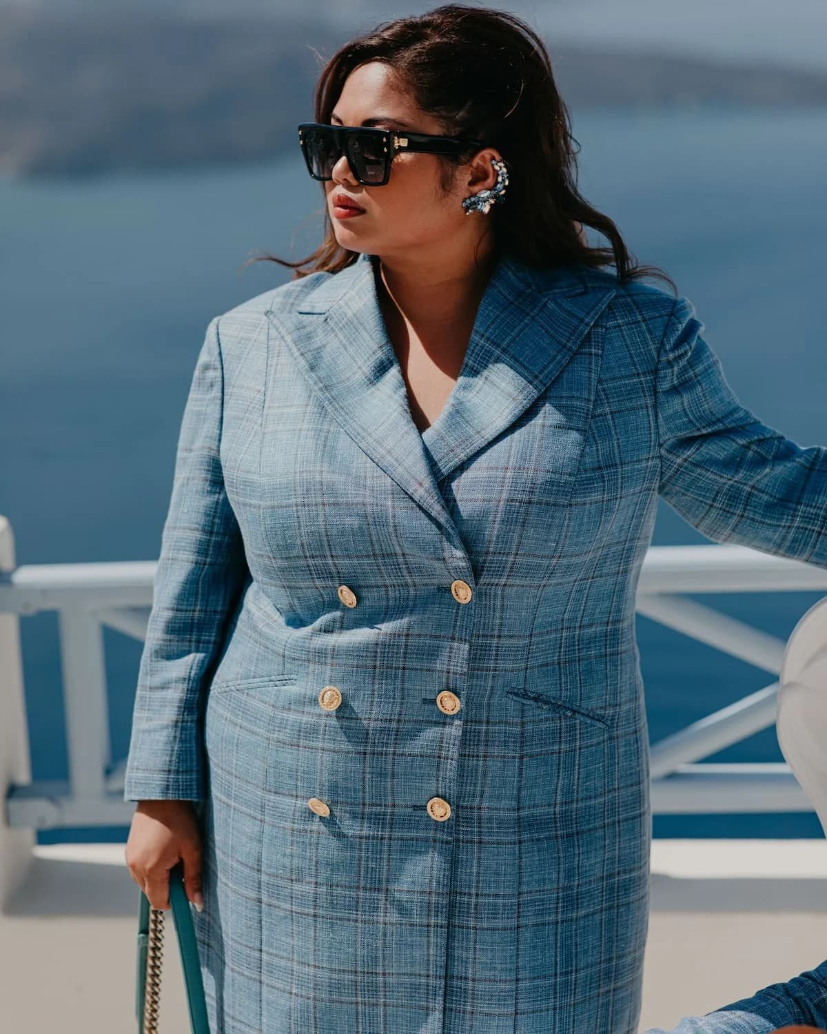 A woman wearing a blue check double-breasted jacket beside the water