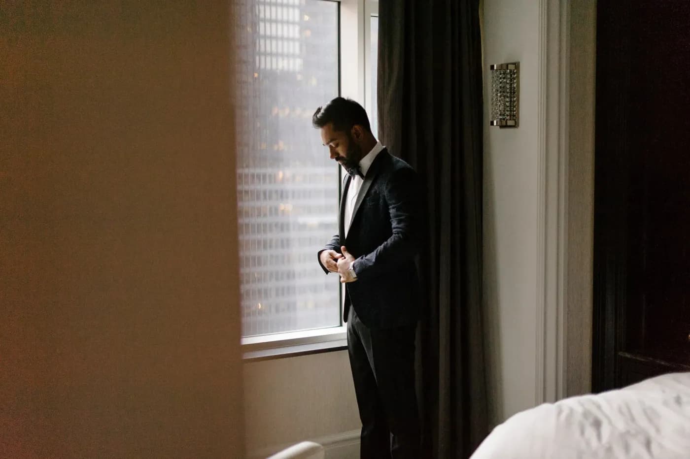 Groom in a black tuxedo standing beside a window before his wedding