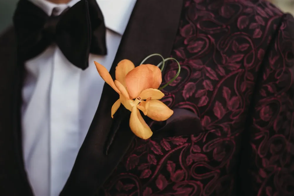 Floral jacquard wedding jacket with a bow tie and orange boutonnière