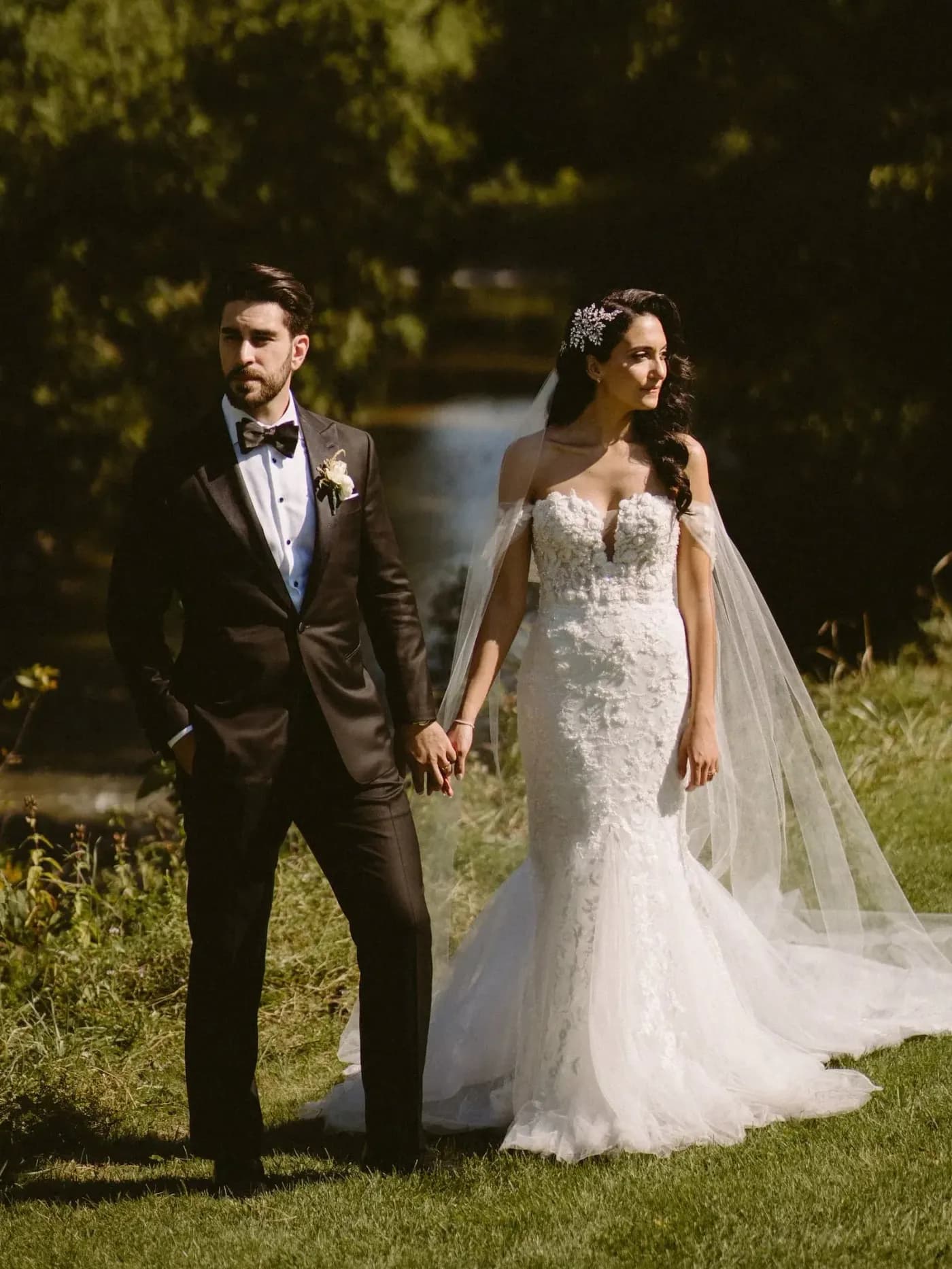 Bride and groom holding hands in a garden, with the groom in a black tuxedo