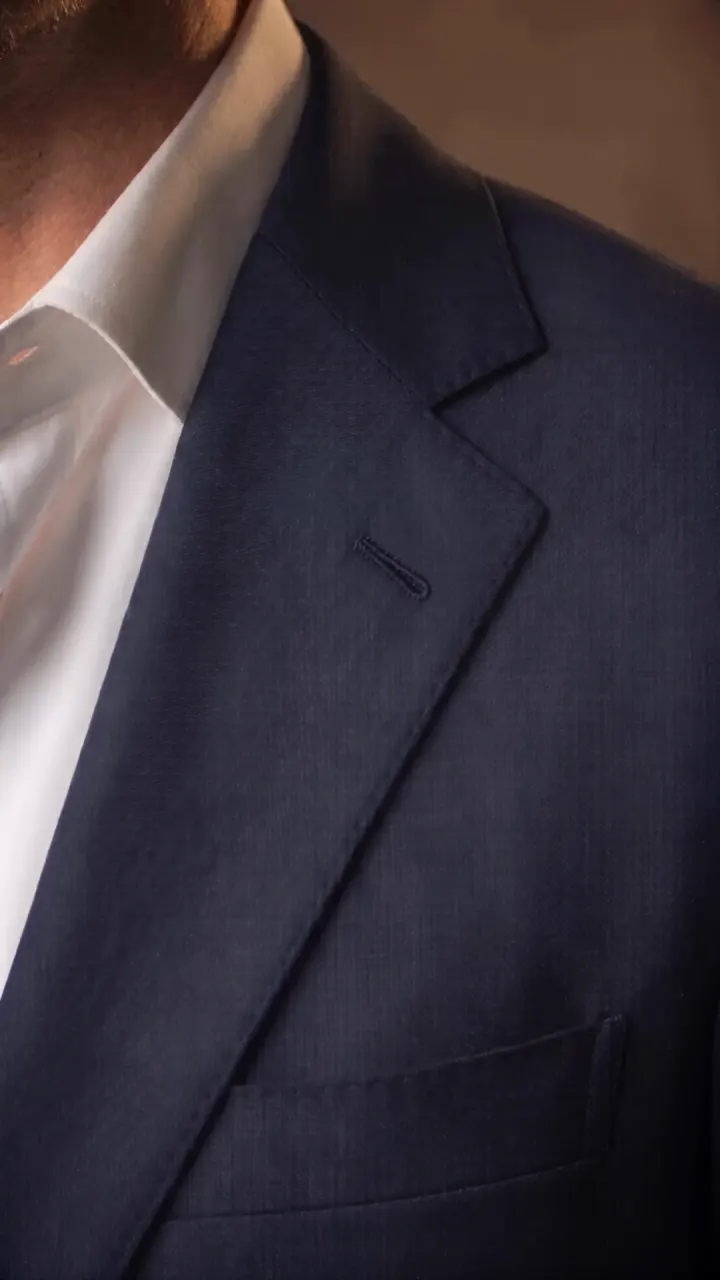 Close view of the navy notch lapel, its soft roll and hand-worked silk buttonhole