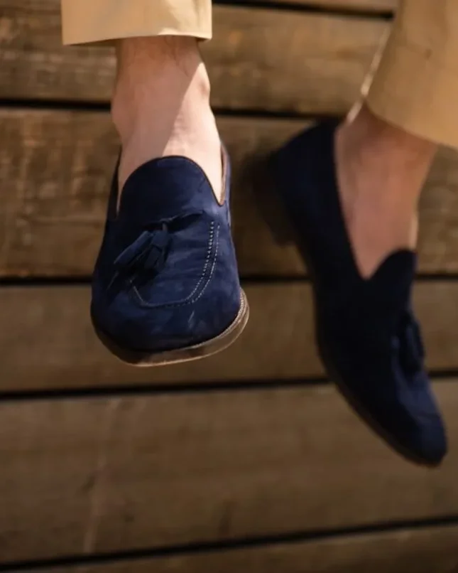 Navy suede tassel loafers worn with light-coloured tailored trousers.